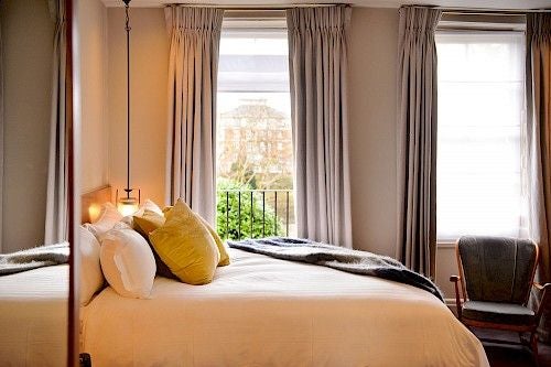 Elegant river-view hotel room with plush white bedding, large windows overlooking a tranquil river, and sophisticated contemporary design at Scenset Riverhouse