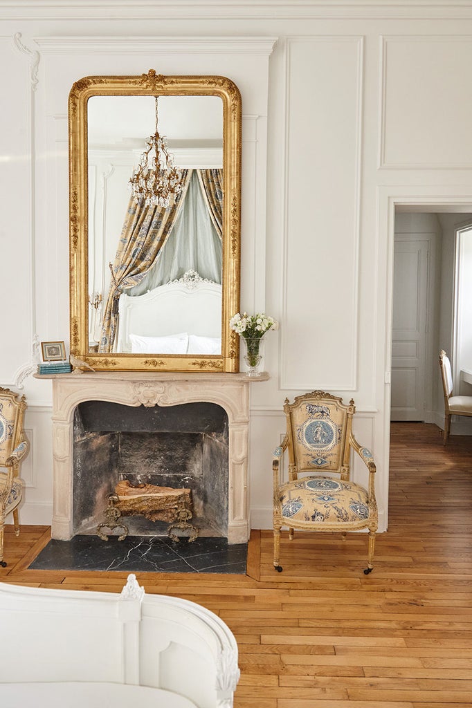 Elegant French château hotel room with ornate crown molding, antique furnishings, lavish king bed, and garden-facing windows with silk drapes