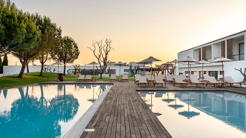 Sleek contemporary hotel building with glass walls reflecting blue sky, surrounded by manicured gardens and modern outdoor lounge areas