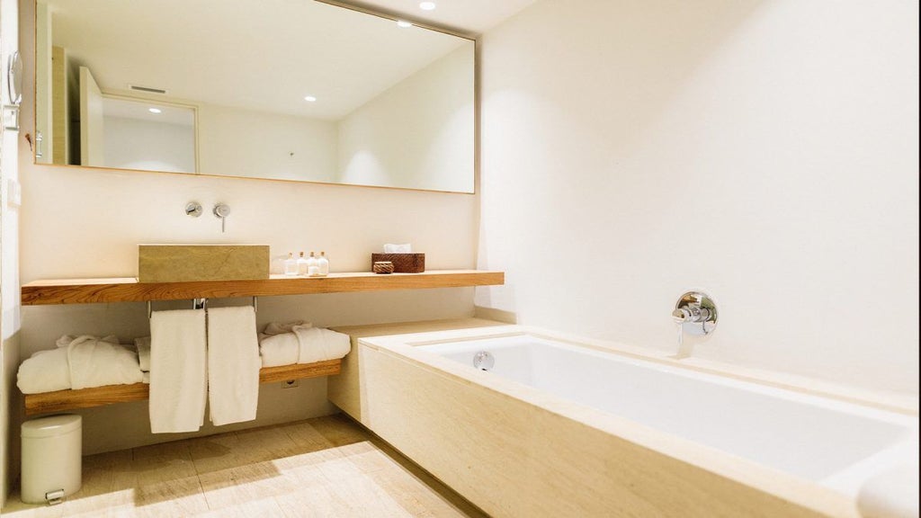 Minimalist white-washed Spanish countryside hotel room with crisp linens, elegant wooden furnishings, and panoramic view of rural Menorca landscape