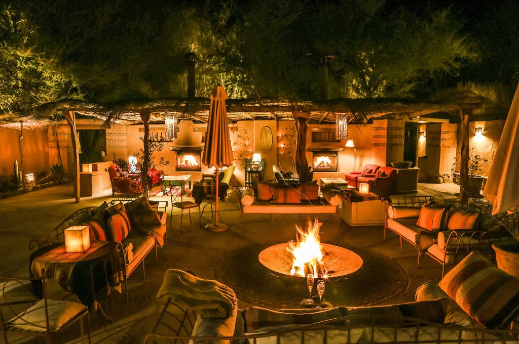 Luxurious desert lodge with adobe walls and thatched roofs nestled among cacti, featuring rustic-chic outdoor seating under wooden beams