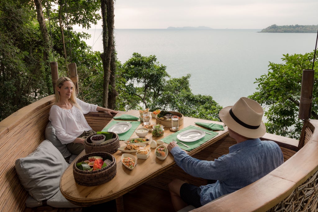 Luxurious overwater villa with private infinity pool overlooking pristine Thai beach, surrounded by lush tropical forest at sunset