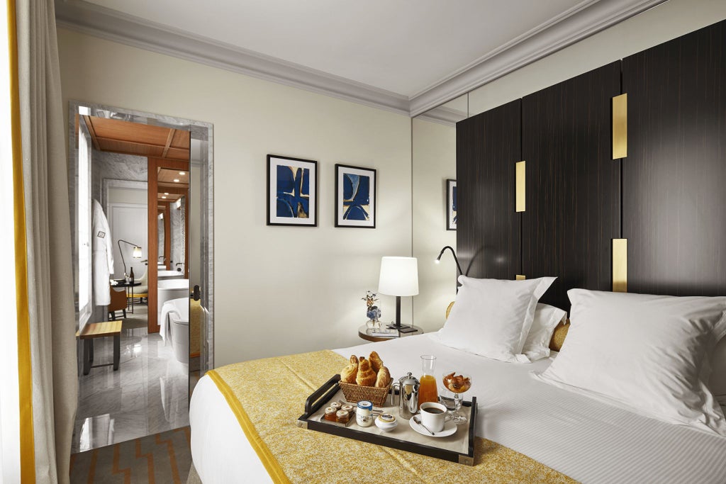 Elegant Paris suite with soft neutral tones, plush king bed, designer furniture, large windows overlooking chic urban streetscape in luxurious Hotel Montalembert