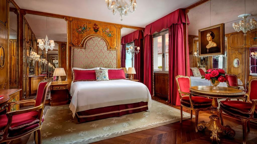 Ornate Venetian hotel room with crystal chandelier, gilded mirrors, antique furniture, and damask-covered walls bathed in warm lighting