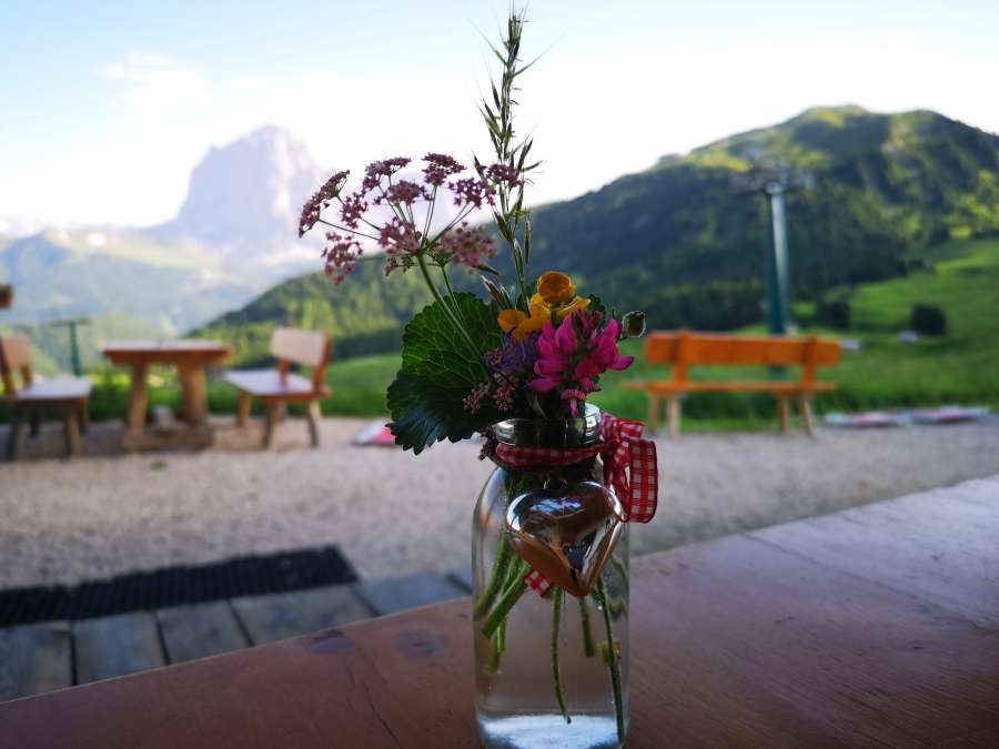 Modern mountain lodge with rustic wooden exterior and floor-to-ceiling windows overlooking dramatic Dolomites peaks at sunset