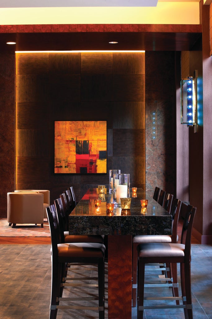 Contemporary glass high-rise hotel in downtown Denver with elegant stone facade, dramatic lighting, and mountain backdrop at sunset