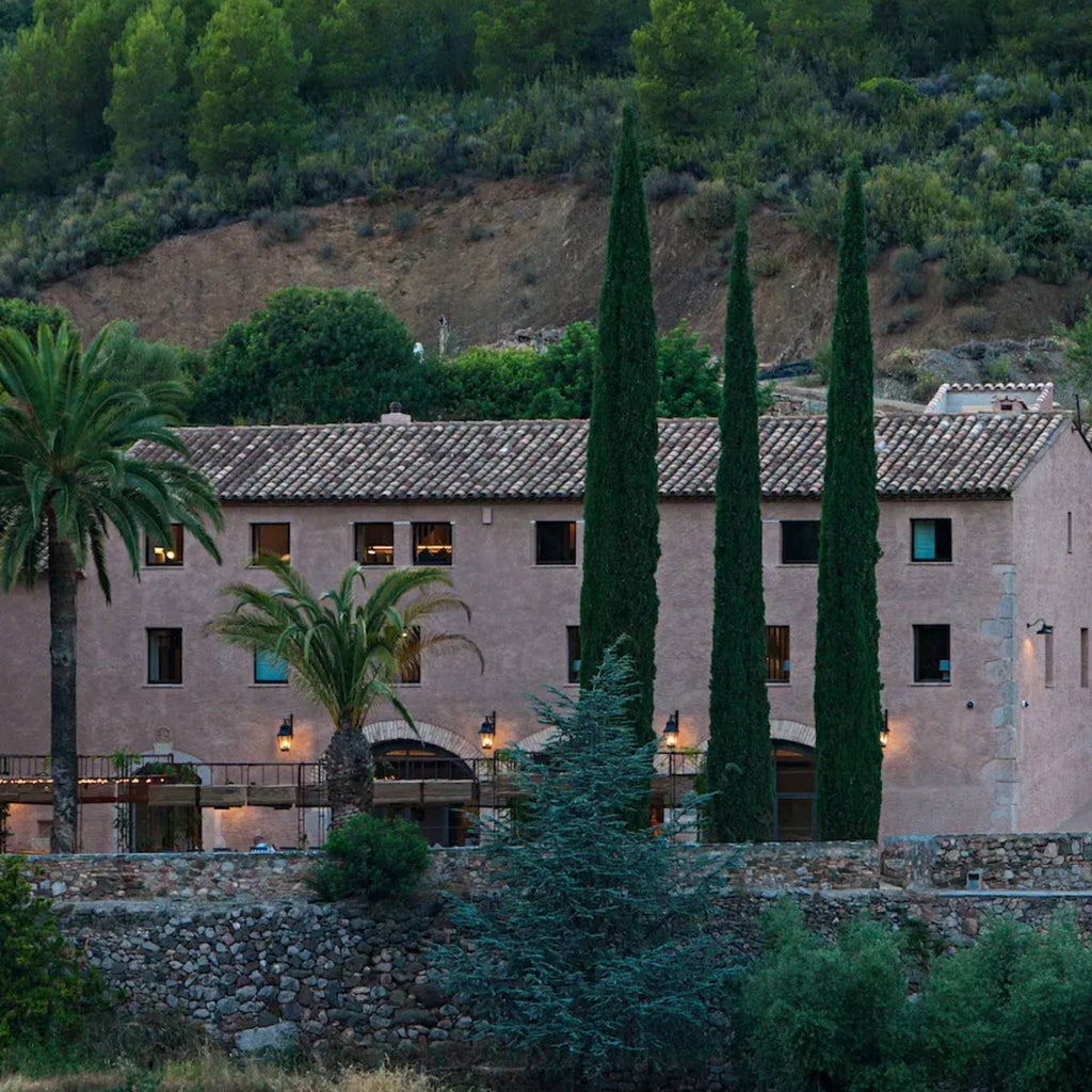 Luxurious Spanish winery hotel nestled among rolling vineyards, featuring elegant stone architecture and golden sunset lighting in scenic countryside landscape