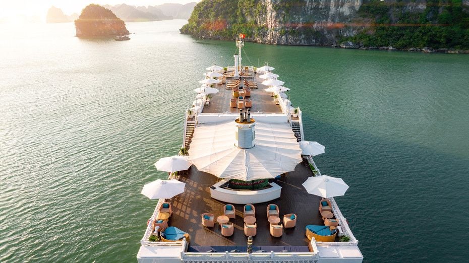 Luxurious Scenset cruise ship on emerald waters of Halong Bay, traditional white sails gleaming against dramatic limestone karsts of Vietnam