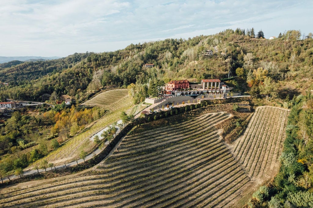 Luxurious Italian hilltop hotel with stone facade, terracotta roof, surrounded by lush Piedmont vineyards and rolling countryside landscape at golden hour