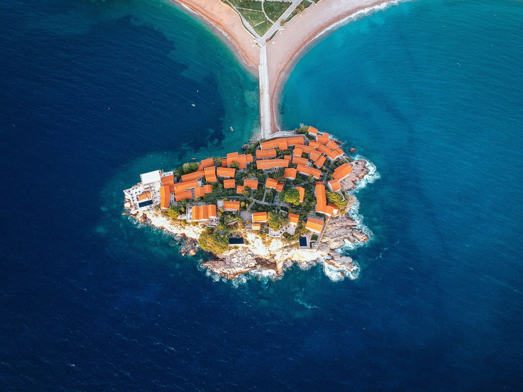 Aerial view of Montenegro's rugged coastline with crystal-clear Adriatic waters, luxury yachts docked in a marina near medieval stone buildings