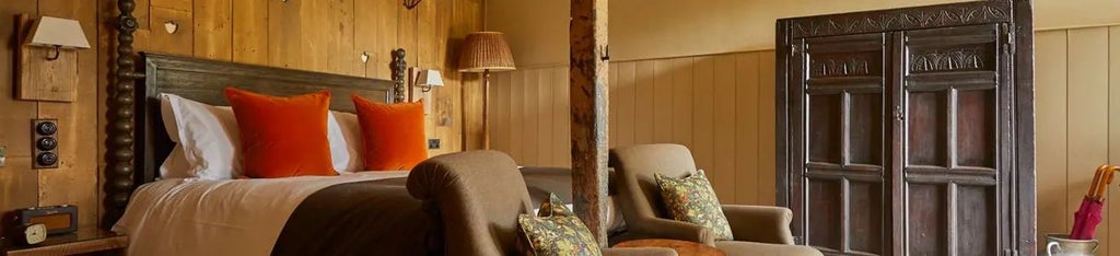 Elegant rustic hotel room with plush white bedding, vintage botanical artwork, and soft natural light streaming through large countryside windows