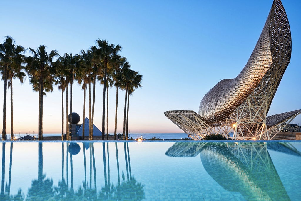 Contemporary glass skyscraper hotel towers over Barcelona coastline, with infinity pool terrace and manicured gardens against blue sky