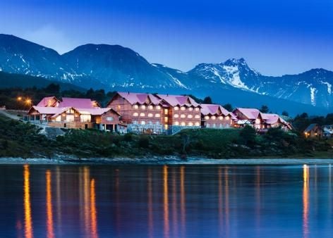 Luxurious waterfront resort nestled in Patagonia, Argentina, with modern architecture, snow-capped mountains, and tranquil waters reflecting golden sunset light