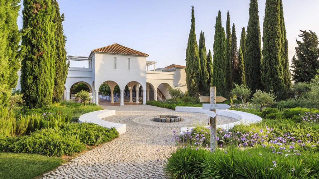 Elegant whitewashed villa hotel in Portugal with terracotta roof, surrounded by manicured gardens and towering palm trees at sunset