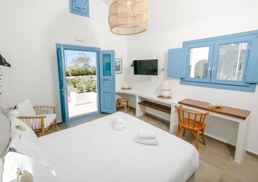 Luxurious Greek villa bedroom with white stone walls, elegant wooden furniture, and panoramic Aegean Sea view through arched windows