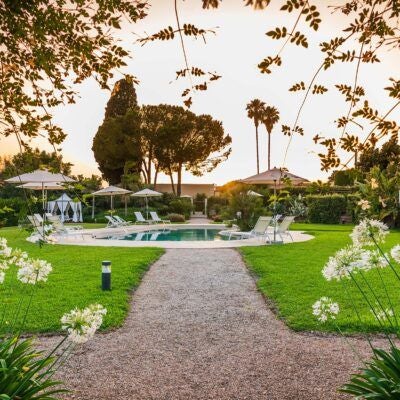 Elegant Sicilian villa with lush gardens, stone pathway, and classic Mediterranean architecture, surrounded by verdant landscape near Syracuse