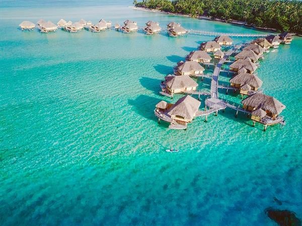 Luxurious overwater villa in Taha'a with private deck, thatched roof, and turquoise lagoon views through floor-to-ceiling windows