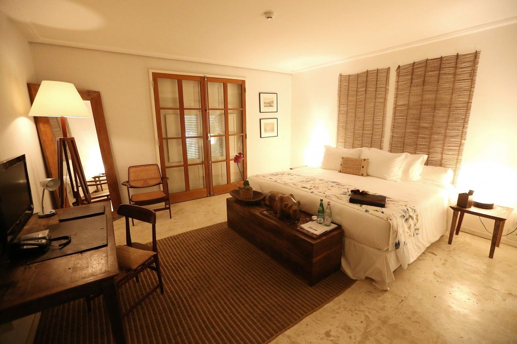 Elegant Brazilian hotel room with luxurious white bedding, wooden floors, and a private balcony overlooking lush scenery in Rio de Janeiro