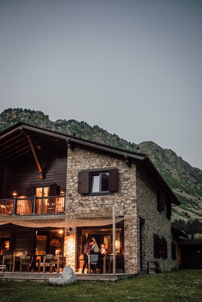 Rustic luxury mountain lodge nestled in Andorran peaks, featuring warm wooden exterior, snow-capped mountain backdrop, and inviting alpine architectural design