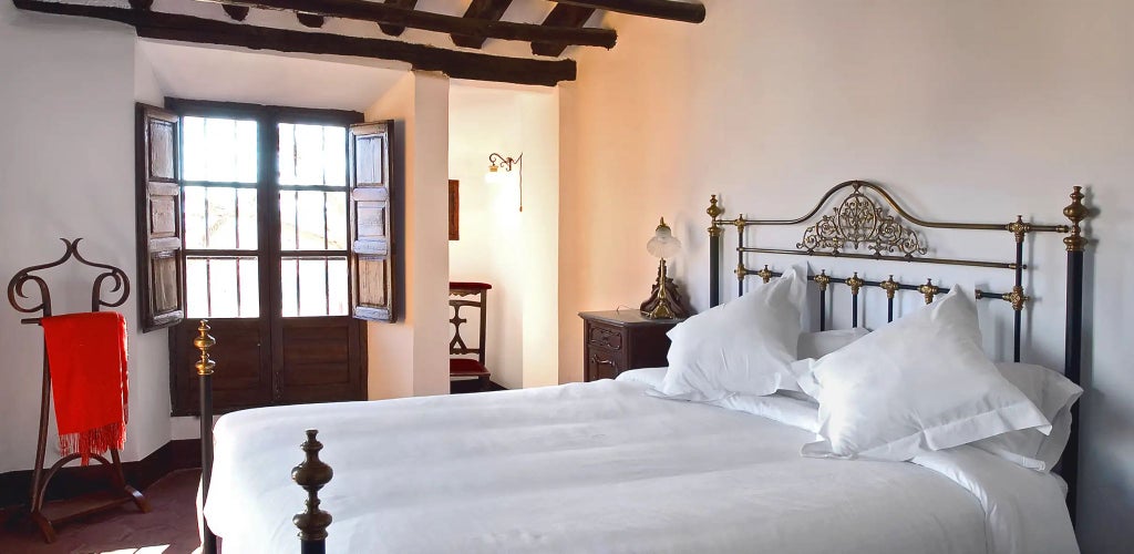 Elegant Spanish countryside hotel room with rustic stone walls, antique wooden furniture, and soft natural light streaming through tall windows