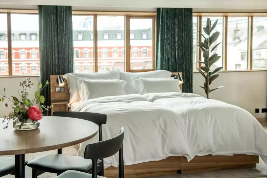 Elegant Norwegian superior suite with modern Scandinavian design, featuring plush king bed, minimalist wood furniture, and expansive city view window