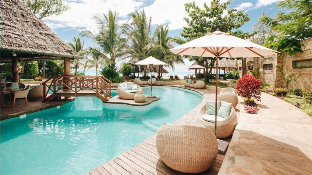 White-sand beachfront resort with thatched-roof villas, infinity pool overlooking turquoise ocean, and swaying palm trees at sunset