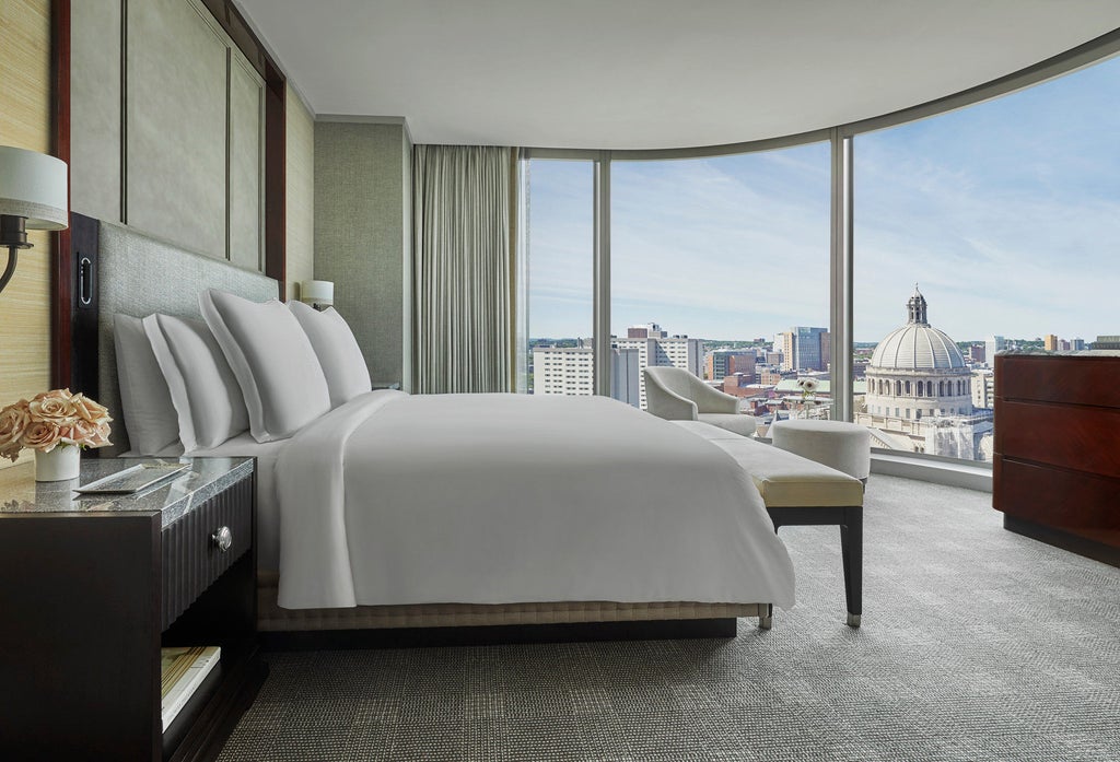 Modern glass skyscraper hotel with curved facade rises elegantly into Boston skyline, reflecting sunlight off its sleek blue-tinted windows