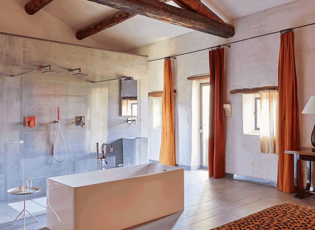 Elegant stone-walled suite with plush white bedding, rustic wooden furniture, and soft natural light in a historic French boutique hotel room