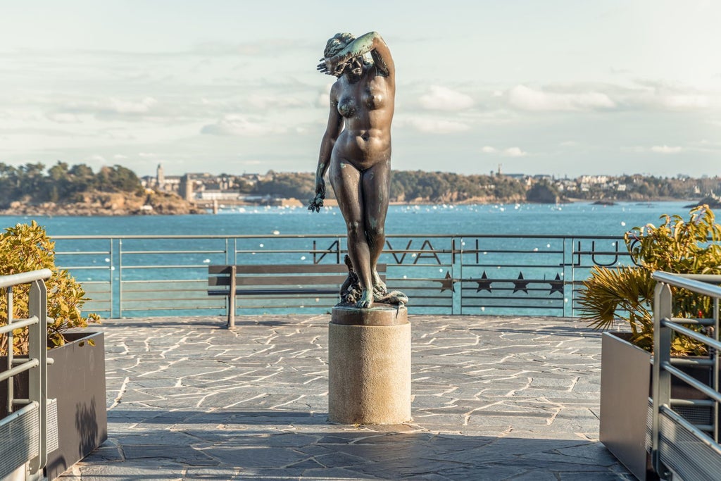 Luxurious coastal hotel perched on rocky cliffs of Brittany, with blue-and-white façade, elegant balconies overlooking azure sea waters near Dinard