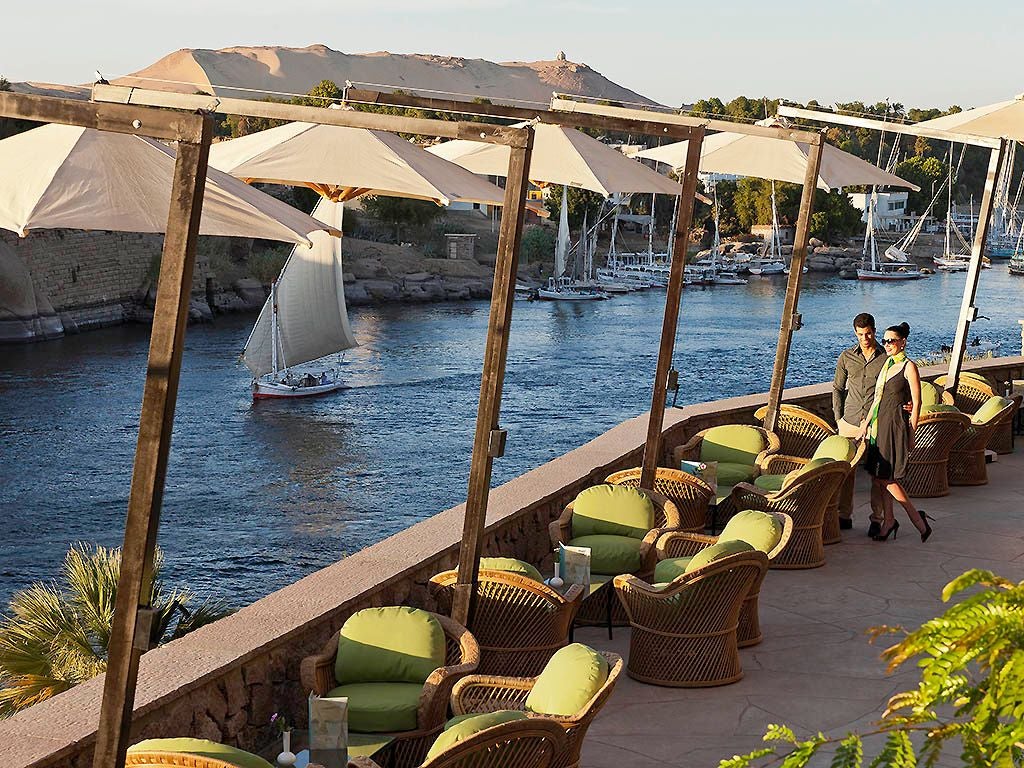 Luxurious historic Sofitel Legend hotel nestled along the Nile River, featuring elegant colonial architecture with palm trees and desert landscape background