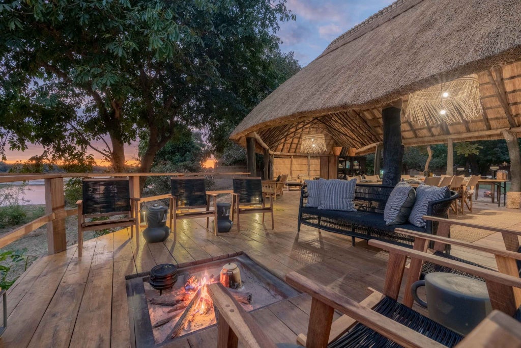 Luxurious safari lodge nestled in South Luangwa National Park, featuring canvas tents with wooden decks overlooking a tranquil river landscape at sunset