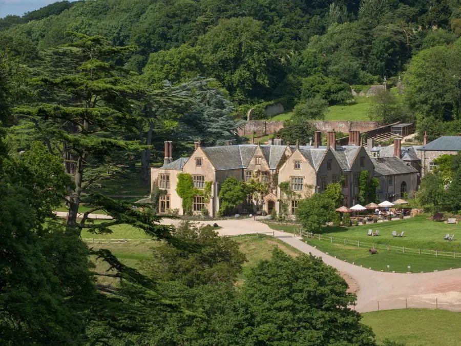 Luxurious coastal hotel nestled in Cornwall, with rustic stone exterior, lush green gardens, and panoramic views of the rugged scenset coastline.