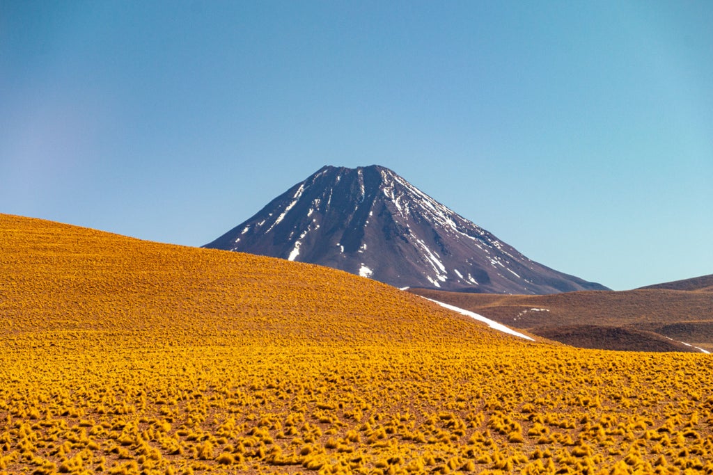 Sand dunes and rocky mountains in Chile's Atacama Desert at sunset, with warm orange light casting long shadows across pristine landscape