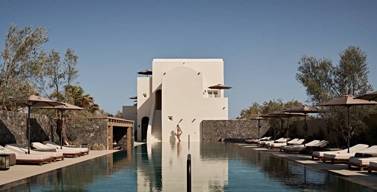 White-washed luxury boutique hotel in Santorini with curved archways, stone walls, and a private plunge pool overlooking the Aegean Sea