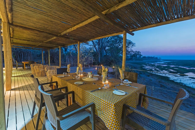 Luxurious safari tent overlooking Linyanti marshlands at sunset, with wooden deck, canvas walls and elegant outdoor furniture