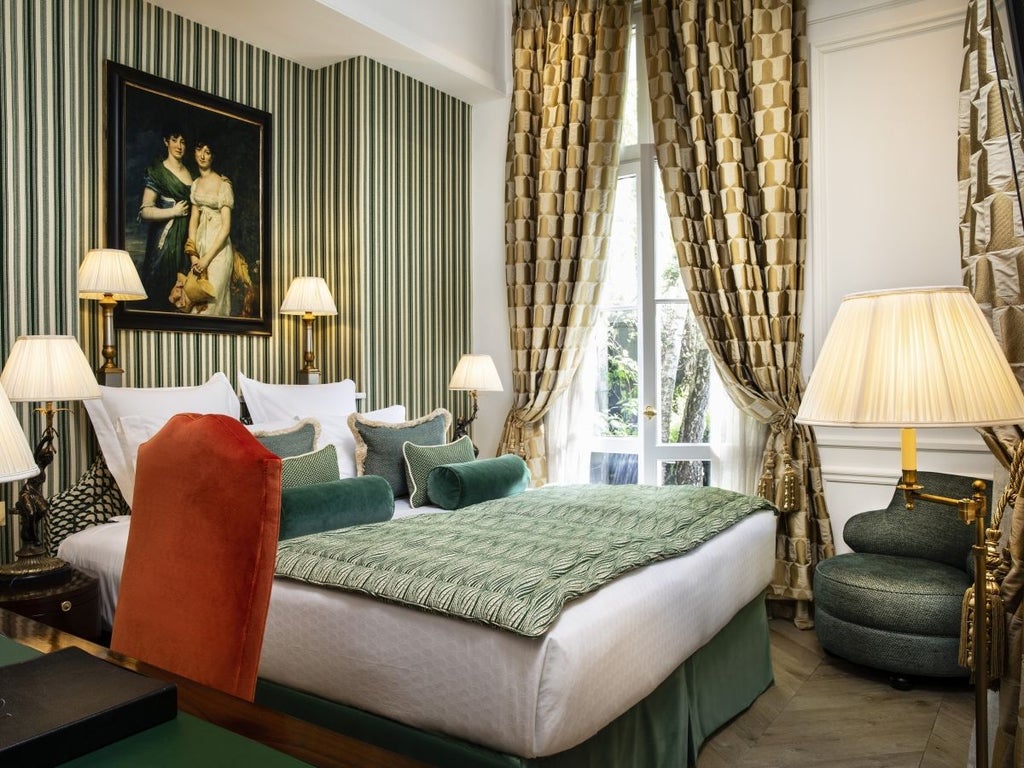 Elegant 17th-century luxury hotel in Paris with ivy-covered stone facade, ornate iron gates, and manicured courtyard garden at dusk