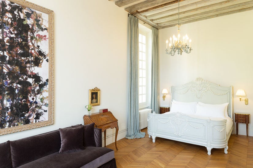 Elegant French château hotel studio with ornate period furnishings, king bed, tall windows overlooking manicured gardens, and refined decor