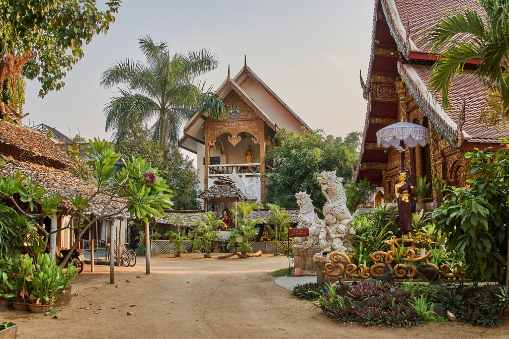 Ancient Wat Chedi Luang temple in Chiang Mai at sunset, with golden spires, ornate architecture and towering palm trees against pink sky