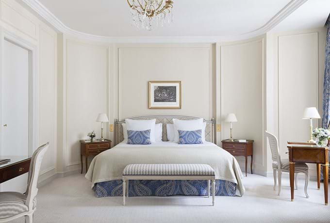 Elegant hotel room with crystal chandelier, silk curtains, period furniture and marble fireplace overlooking Parisian courtyard garden