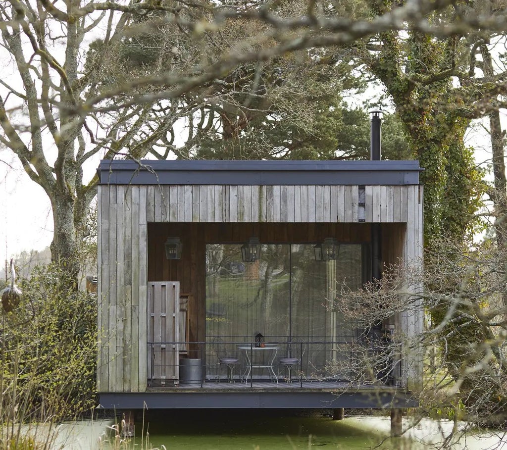 Luxurious forest cabin at Lime Wood with rustic wooden interiors, plush king bed, large windows overlooking lush greenery, and elegant contemporary design