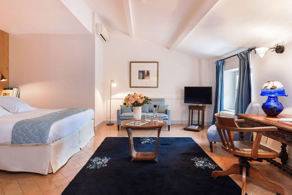 Elegant stone-walled French hotel room with antique furniture, plush white bedding, and soft natural light streaming through arched windows