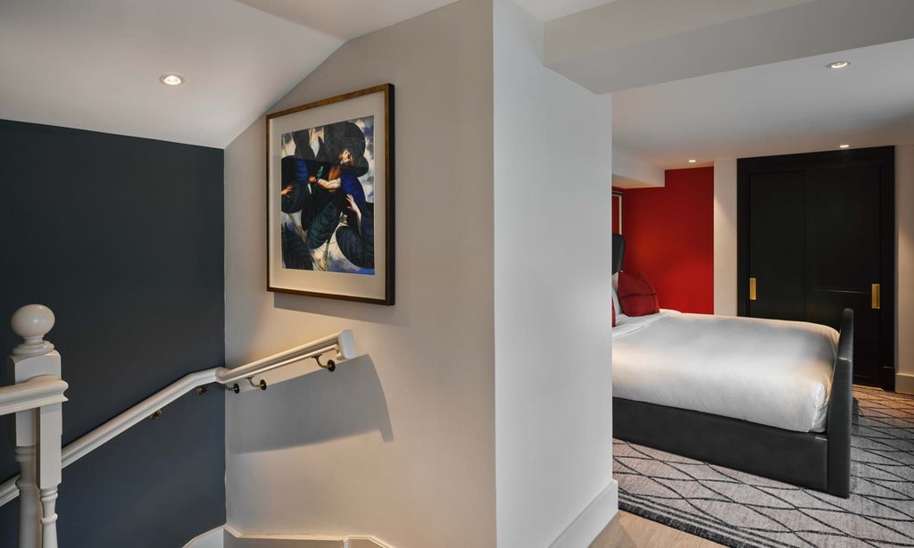 Elegant, spacious loft suite with modern British design, featuring plush king bed, contemporary artwork, and expansive city-view windows at luxury townhouse hotel