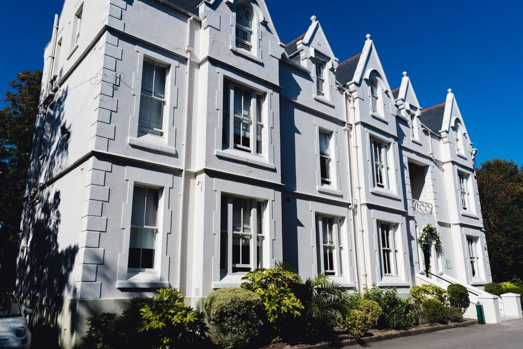 Elegant green facade of a luxury boutique hotel with Victorian architectural details, nestled in a charming urban landscape with pristine windows and manicured entrance