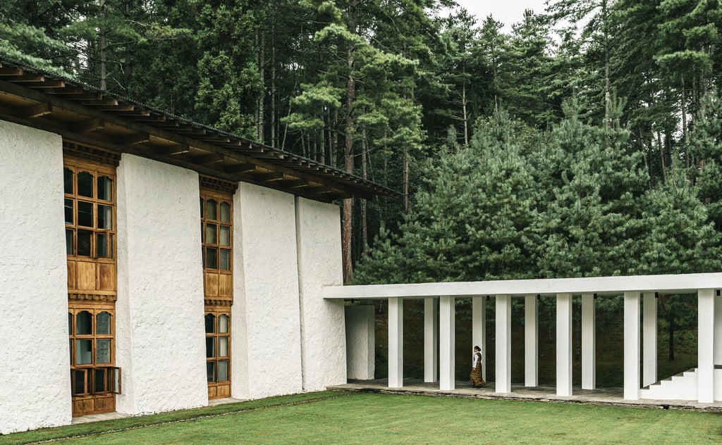 Traditional Bhutanese whitewashed lodge nestled in blue pine forest, featuring stone courtyard and wooden beams with mountain backdrop