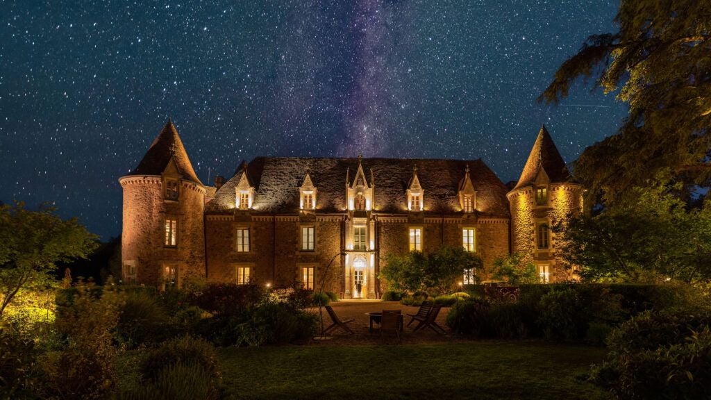 Luxurious French château-style hotel nestled amid lush green countryside, featuring elegant stone architecture and tranquil lake reflections at sunset