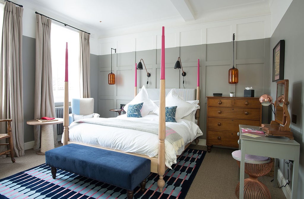 Elegant coastal hotel room at The Swan Southwold, featuring plush white bedding, soft neutral tones, and large window with natural light overlooking seaside landscape