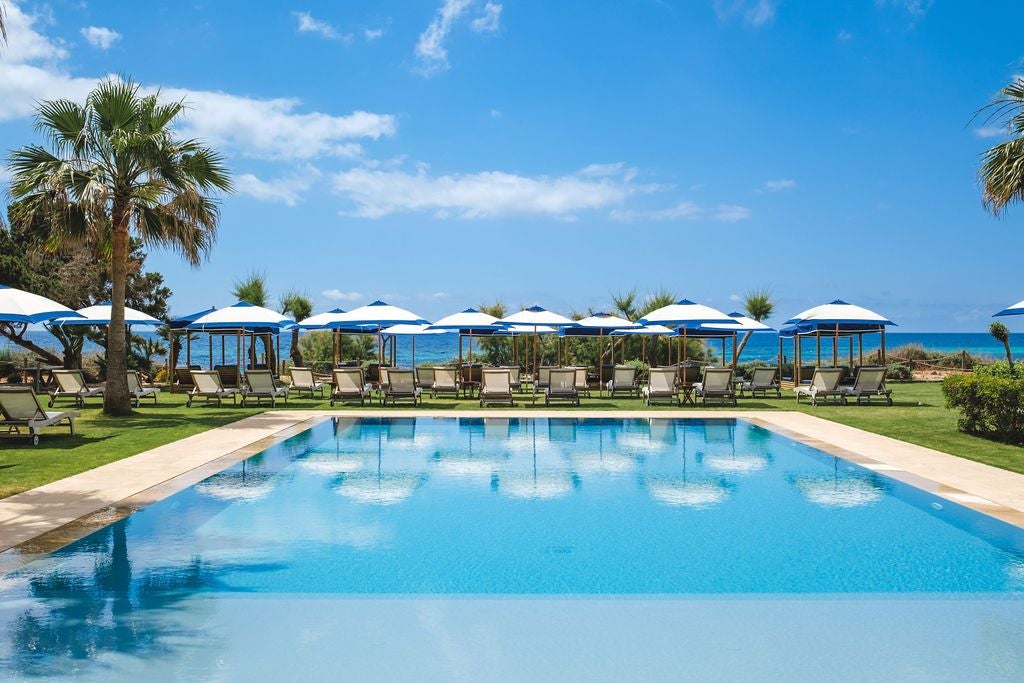 Elegant white-washed Spanish coastal hotel with minimalist design, infinity pool overlooking turquoise Mediterranean waters and rocky shoreline at sunset