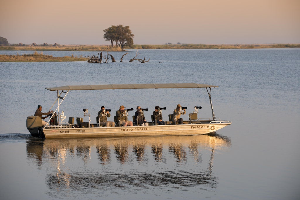 Luxurious white canvas safari tent nestled among acacia trees at sunset, overlooking Chobe River with lantern-lit pathways