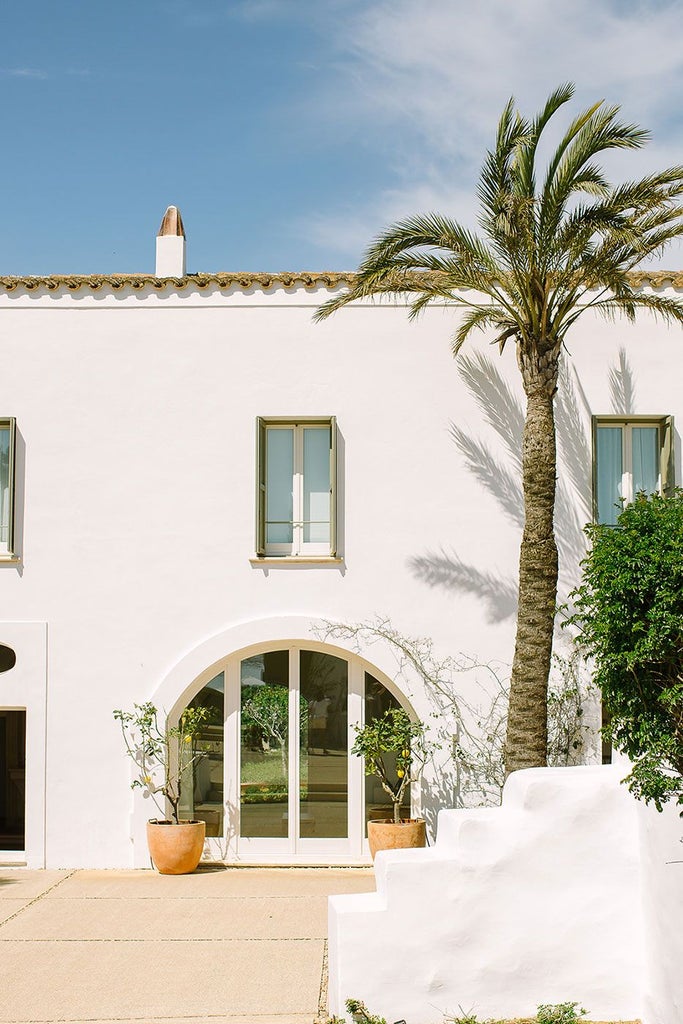 Whitewashed luxury boutique hotel nestled in Menorca's countryside, featuring rustic stone walls, elegant pool, and Mediterranean landscape