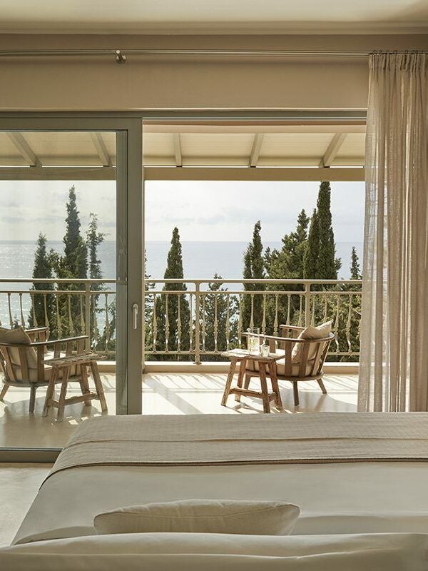 Luxurious modern hotel room with minimal white decor, large windows overlooking azure Kefalonian coastline, minimalist design with crisp linens and sleek furnishings